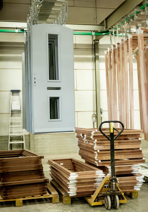 Gespoten voordeuren aan de kettingen boven gestapelde houten ramen op pallets