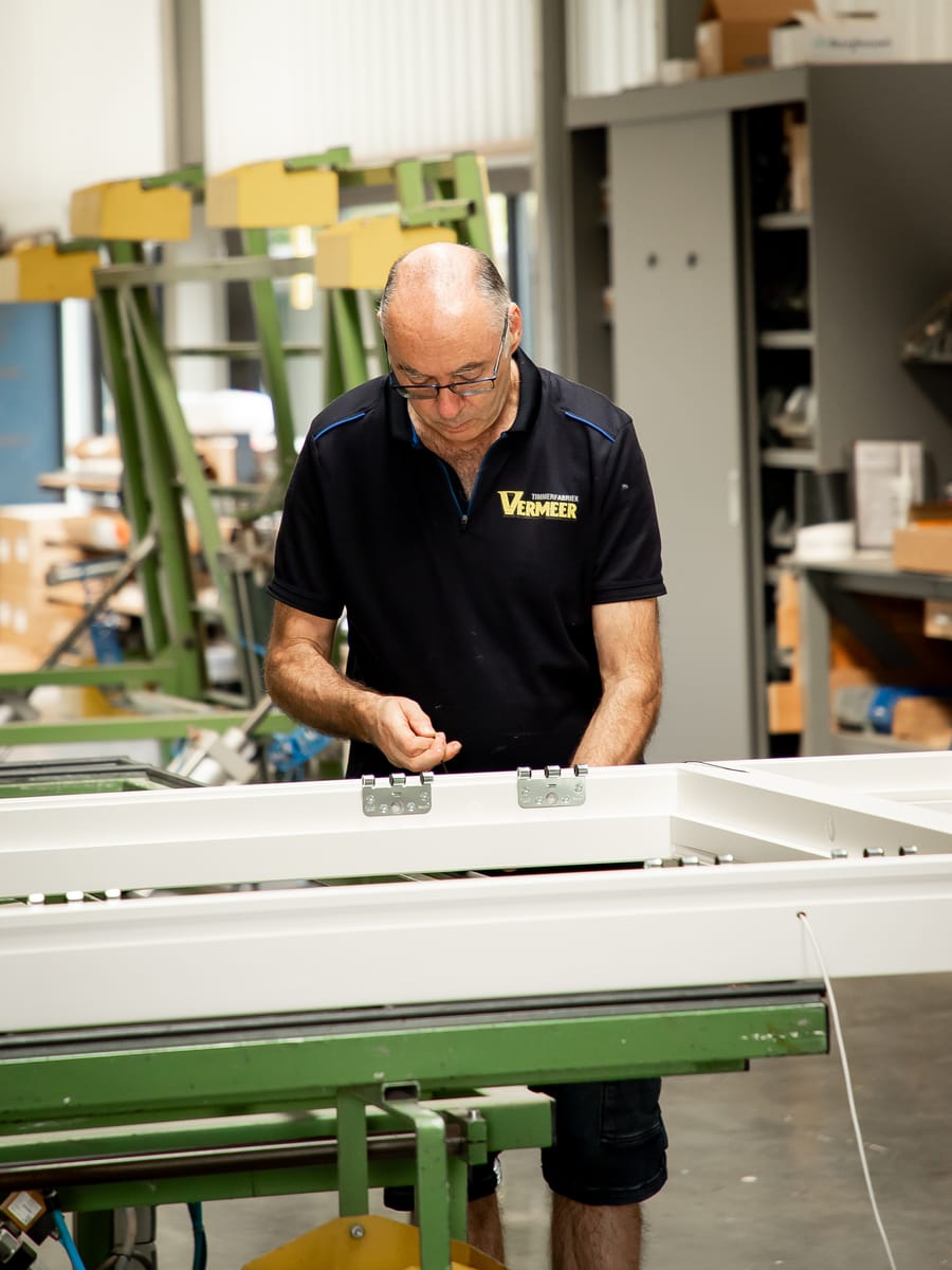 Medewerker monteert beslag op een wit raam op de afmontagetafel